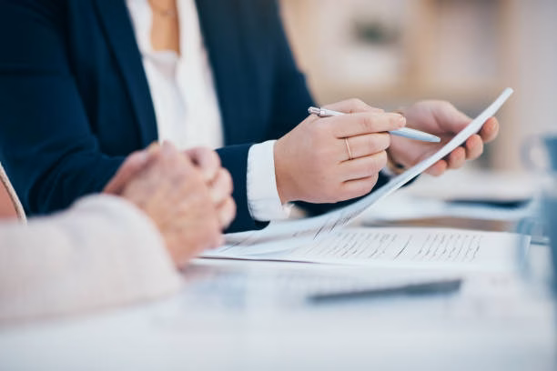 Hands working, reading and writing on business meeting notes in an office boardroom. Closeup view of corporate executive team doing work. Management group looking through finance data together